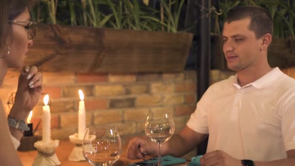 Молода пара сидить на столі зі свічкою під час романтичної вечері в ресторані. Чоловік і жінка п'ють вино під час вечірньої вечері в романтичному кафе. Офіціантка, що обслуговує пару в ресторані . — стокове відео