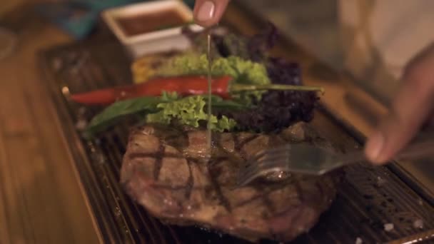 Mão masculina cortando carne grelhada com faca e garfo enquanto jantar no restaurante churrasco. Homem cortando carne churrasco no café de perto . — Vídeo de Stock