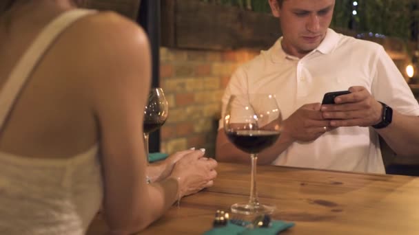 Anak muda menggunakan ponsel sementara kencan romantis di kafe malam. Tampan pria mencari smartphone di meja di makan malam romantis dengan anggur merah di restoran . — Stok Video