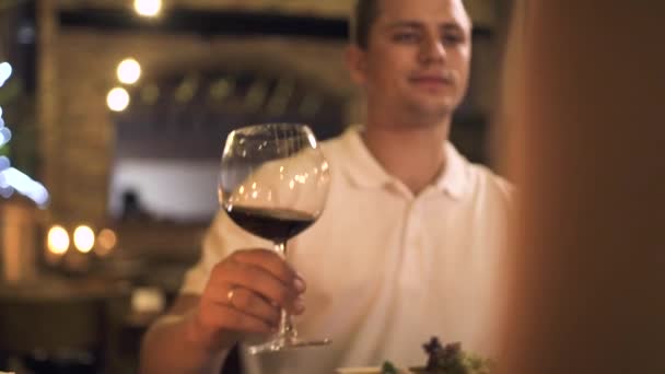 Pohledný muž mluví toast s sklenka na červené víno na romantickou večeři pro dva v restauraci. Pár v lásce pití vína ze skla na romantické rande v elegantní restauraci. — Stock video