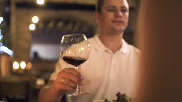 Hombre guapo hablando tostadas con copa de vino tinto en la cena romántica para dos en el restaurante. Pareja enamorada bebiendo vino de copa en cita romántica en elegante restaurante . — Vídeos de Stock