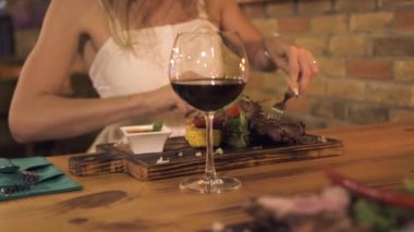 Genç kadın Barbekü restoranda akşam yemeği sırasında bıçak ve çatal ile ızgara et kesme. Kadın yeme et mangal kafede yakın çekim.