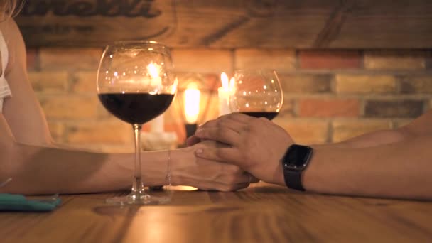 Casal romântico de mãos dadas à mesa com velas e copo de vinho. Homem e mulher de mãos dadas na data romântica com velas no restaurante à noite . — Vídeo de Stock
