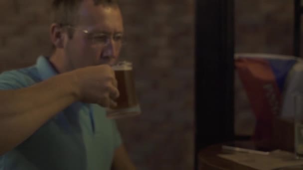 Handsome man enjoying fresh beer in bar pub. Young man drinking beer from mug in sport bar while resting after hard day. — Stock Video