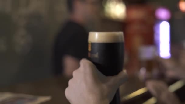 Młody człowiek picia ciemnego piwa ze szkła w pub bar z bliska. Portret przystojny mężczyzna, popijając zimne piwo w sport bar. — Wideo stockowe