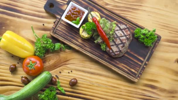 Barbecue viande steak composition vue de dessus. Steak grillé au piment rouge, aux herbes, au maïs et à la sauce tomate sur une planche de bois. Fond alimentaire sur l'espace de copie en bois. Nutrition saine et concept de régime alimentaire . — Video
