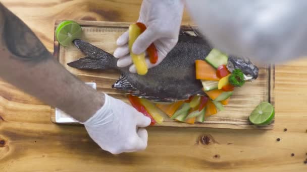 Шеф-повар готовит украшение жареной рыбы из свежих овощей на деревянном фоне. Дизайн и дизайн продуктов питания. Жареная рыба с овощным гарниром в ресторане морепродуктов . — стоковое видео