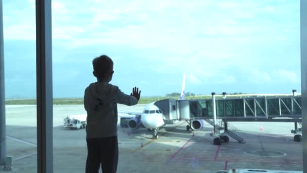 Menino olhando para janela esperando avião na sala de embarque no aeroporto. Menino olhando para aeronaves da janela do terminal do aeroporto na área de espera. Voo aéreo e transporte . — Vídeo de Stock