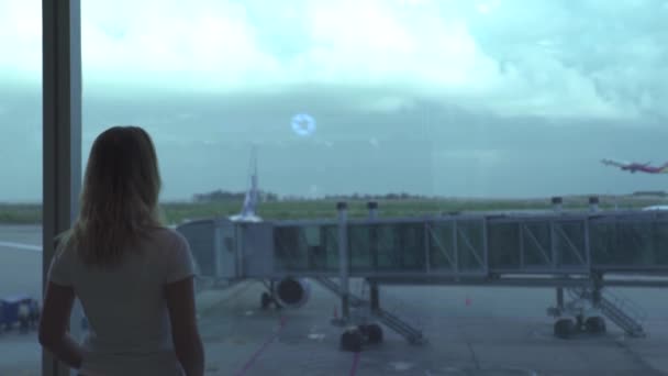 Travling woman looking to airplane from airport window while waiting in departure lounge. Woman tourist looking to aircraft from airport terminal window on waiting area. Travel and tourism concept. — Stock Video