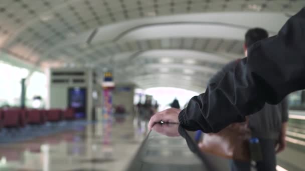 Мужская рука на перилах в зале ожидания аэропорта. Мужчина стоит на движущейся дорожке для транспорта внутри современного бизнес-центра, торгового центра . — стоковое видео