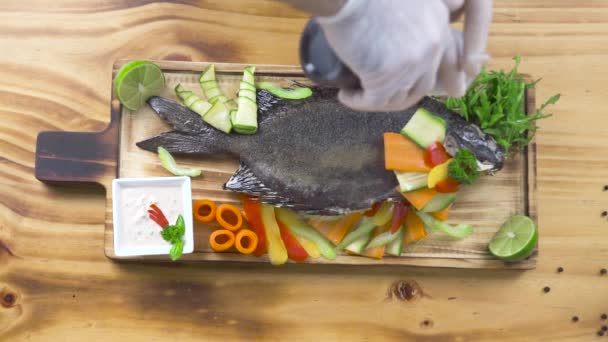 Pesce alla griglia con verdure nel ristorante di frutti di mare. Cuoco cuoco versare salsa su pesce fritto con verdure fresche su sfondo di legno. Food design e styling. Composizione degli alimenti . — Video Stock