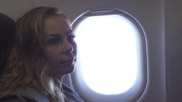 Portrait jeune femme sur fond de fenêtre d'avion. Fille bouclée regardant la fenêtre de l'avion voler dans le ciel. Femme passager à l'intérieur de l'avion volant . — Video