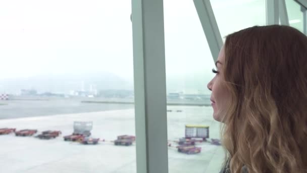 Mulher viajante olhando para a janela do terminal do aeroporto em avião na sala de embarque. Mulher turista olhando para janela enquanto espera avião no terminal do aeroporto. Viagens e turismo . — Vídeo de Stock