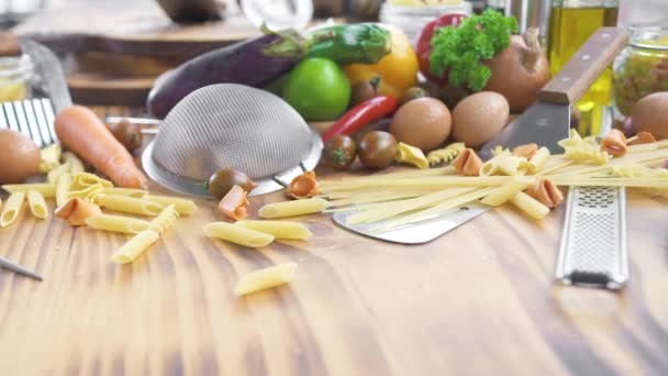 Italské potraviny ingredience na dřevěné pozadí. Těstoviny složení potravin, makarony, zelenina, olej, koření na kuchyňském stole. Složení s raw italské těstoviny, zelenina, olivový olej a bylinky. — Stock video