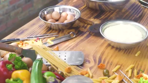 台所のテーブルに食品成分。鶏の卵、小麦粉、木製のテーブルの上に食べ物を調理するための新鮮な野菜。イタリアのパスタと木製の背景に生の野菜とマカロニ。料理のコンセプト. — ストック動画