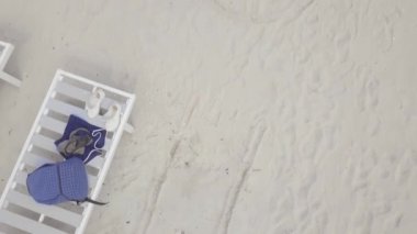 Kumlu plajda havadan manzaralı şezlong. Bikinili genç kadın şezlongda yatıyor ve deniz plajında cep telefonu kullanıyor.