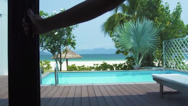 Point of View uitgang naar veranda met zwembad op zee strand landschap. Uitzicht vanaf raam op zwembad op luxe villa op zee strand, blauw water en Palm Tree achtergrond. — Stockvideo