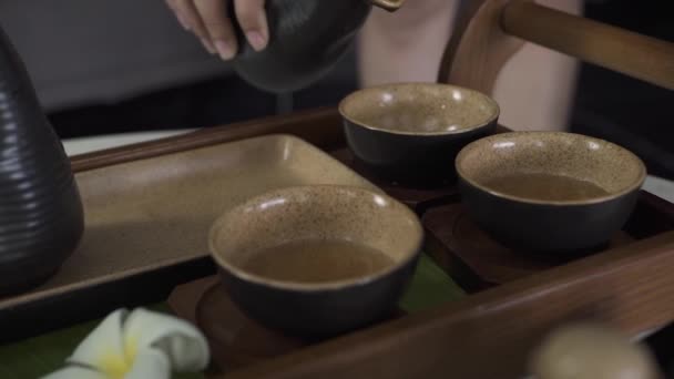 伝統的な中国の茶道をしながら、ボウルにやかんからお茶を注ぐ女性の手。日本の式典中にティーポットからカップに緑茶を注ぐ女性. — ストック動画