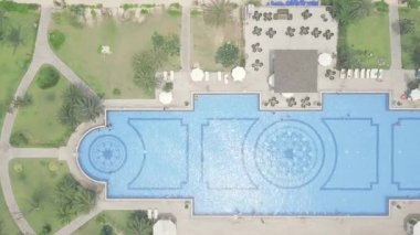 Mavi yüzme havuzu, şemsiye ve yeşil çim lüks tatil otel görünümünde yukarıdan uçan drone. Otelde salon alanında havadan büyük yüzme havuzu ve şemsiyeler ve şezlonglar manzarası.