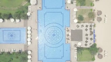 Lüks tatil oteli havadan görünümünde mavi yüzme havuzu, şemsiye ve yeşil çim. Büyük yüzme havuzu ve şemsiye ve şezlong salon alanında otel görünümünde uçan drone yukarıdan.
