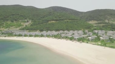 Yeşil dağlar ve mavi su manzara üzerinde deniz kıyısında yüzme havuzları ile lüks villa ve konaklar. Deniz plajı ve yeşil dağlık arka plan üzerinde Resort oteller. Havadan görünüm.