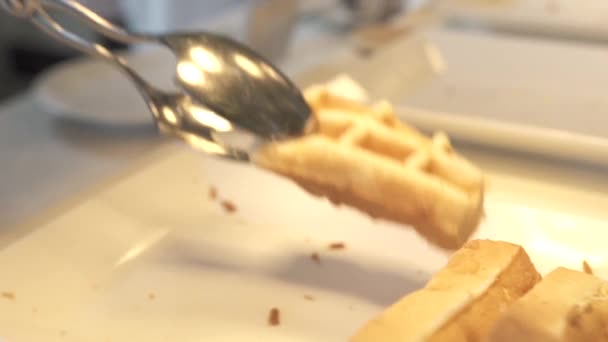 Рука бере бельгійські вафлі і кладе на білу тарілку на шведський стіл в готельному ресторані. Солодкі печені вафлі на ранковий сніданок. Концепція десертної їжі. Їжа з пастеризацією. Дієта і харчування . — стокове відео