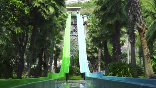 Människor som har kul ridning på vattenrutschbana på Aquapark på sommarlovet. Utomhus vattenpark med rör och diabilder på gröna palmträd landskap. — Stockvideo