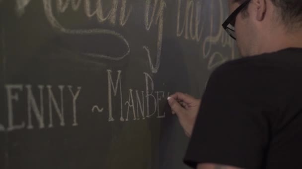 Junger Mann zeichnet Kreide auf Tafel in Kneipe. Kellner schreibt Speisekarte auf Kreidetafel im Restaurant. Zeichnung Menü Preis im Café. — Stockvideo