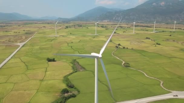 緑のフィールドと山の風景の上にきれいな再生可能エネルギーを生成する風力発電所。現場でのドローンビュー風車。風力発電所のタービン。代替エネルギーと生態学の概念 — ストック動画