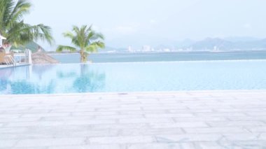 Palmiye ağaçları ve deniz manzarası üzerinde mavi sonsuzluk havuzu. Büyük şehir ve mavi deniz manzara üzerinde resort otel lüks yüzme havuzu.