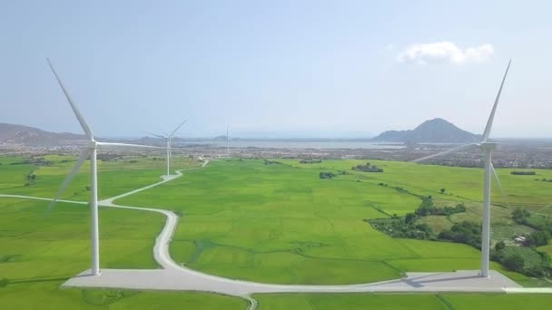農業分野でのエネルギー発電所の風車。緑のフィールド、海と山の風景の上に空中ビュー風力発電ファーム。再生可能エネルギーの代替エネルギーの発電. — ストック動画