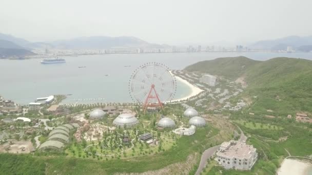 Roue de ferris géante dans un parc d'attractions sur mer et paysage urbain moderne. Parc d'attractions avec grande roue ferris sur fond de mer, de montagne et de ville d'été . — Video