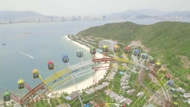 Colorful ferris wheel in amusement park on sea, mountain and modern city landscape aerial view. Amusement park with large ferris wheel and aqua park from drone above. — Stock Video