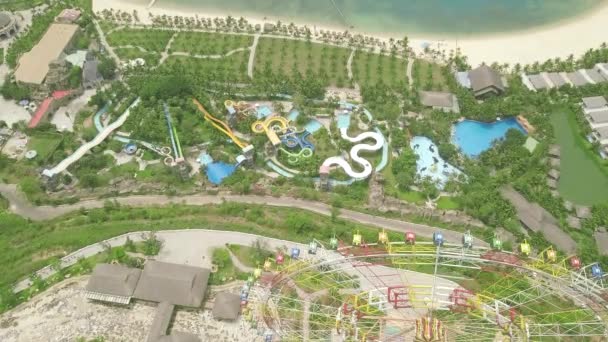 Drone view colorful water slide in amusement aquapark on blue sea beach. People having fun riding on slides in outdoor water park on green palm tree landscape. Summer activity. — Stock Video