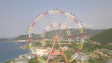 Deniz ve dağ manzarası üzerinde eğlence parkı renkli dönme dolap havadan görünümü. Uçan drone yukarıdan büyük dönme dolap manzaralı eğlence parkı.