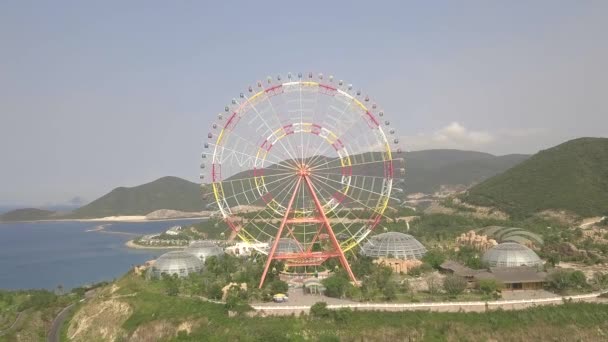 Різнокольорове колесо Феррі в парку розваг на морі та гірському ландшафті з видом на повітря. Парк розваг з великим паромним видом зверху на літаючий безпілотник . — стокове відео