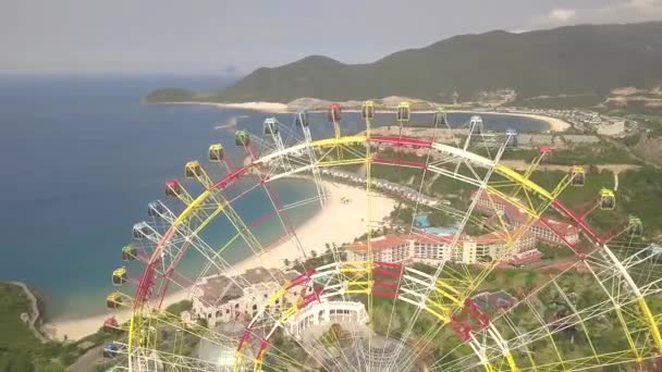 V zábavním parku na moři a horských krajinných horách se Drone zobrazí barevné kolo. Zábavní park s velkým železištěm na pozadí zelených vysočin. Letecký pohled. — Stock video