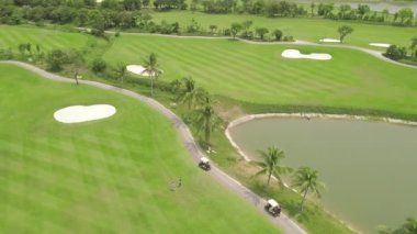 Golfçü uçan drone yeşil golf sahası üst görünümünde oynuyor. Golf kulübü, araba ve göl manzara yeşil alanda havadan görünümü insanlar. Spor ve hobi kavramı.