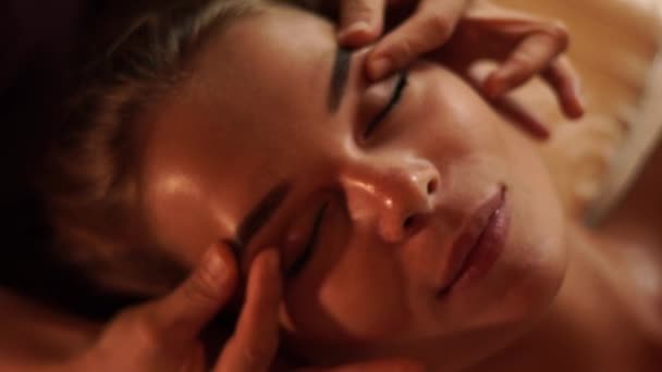 Faccia la giovane donna che riceve il massaggio della pelle in salone di centro benessere di bellezza. Close up ritratto donna ottenere massaggio al viso in studio spa cosmetica. Cura della pelle, concetto di bellezza . — Video Stock