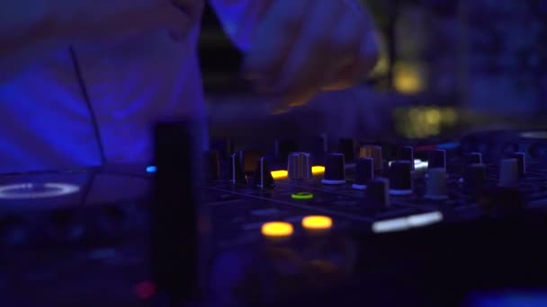 ナイトクラブのダンスパーティーでサウンドコンソールtで音楽を演奏するDJの手。ディスコパーティーのためのDJミキサープレーヤーとサウンドコンソール。ディスクジョッキーコントローラと色付きの照明付きミキシングデッキ. — ストック動画