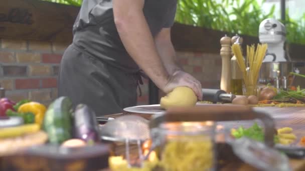 Homem cozinheiro fazendo massa para massas italianas na cozinha. Chef cozinheiro amassar massa de farinha em mesa de madeira para pizza tradicional. Fundo alimentar. Cozinhar produtos de padaria, pastelaria, conceito de comida . — Vídeo de Stock