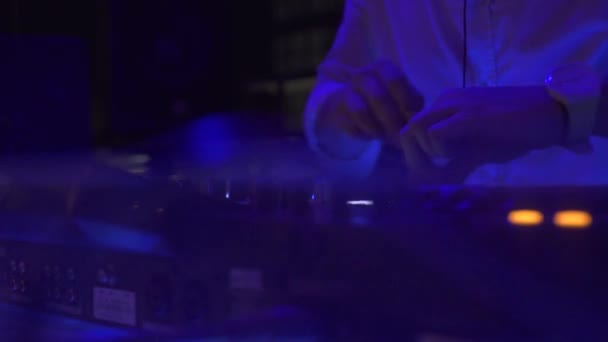 Man DJ gra muzykę taneczną na konsoli dźwiękowej w klubie nocnym party. DJ kontroler do mieszania muzyki i kolorowych świateł w nocnym klubie. Talerz Jockey i konsola do mieszania na imprezę taneczną. — Wideo stockowe