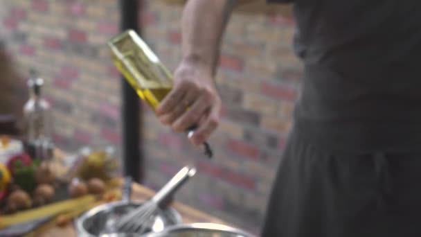 Chef-kok het gieten van olijfolie uit fles tijdens het koken salade op bakstenen achtergrond. Mannelijke hand nemen olijfolie fles terwijl voedselbereiding op keuken gerechten. Koken gezond voedsel concept. — Stockvideo
