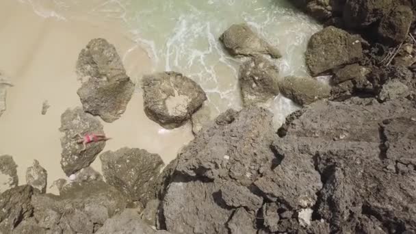 Mujer joven relajándose en piedra y salpicando las olas del mar en la playa de arena. Paisaje aéreo hermosa mujer en la playa tropical mientras salpica el mar. Drone vista paraíso isla y océano turquesa . — Vídeos de Stock