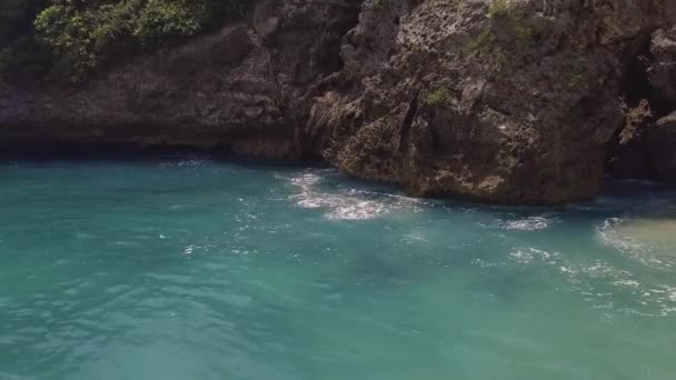 Blaues Meerwasser und felsige Klippenlandschaft. Meereswellen, die mit Schaum und Gischt zum Klippenberg plätschern. türkisfarbenes Meerwasser und felsige Insel. bali, indonesien. — Stockvideo