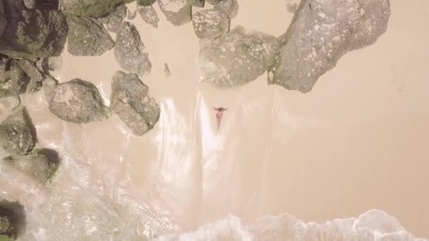 Attractive woman lying on sandy beach in sea waves with foam and spray drone view. Aerial view woman relaxing on tropical beach. Transparent ocean water splashing on shore. — Stock Video