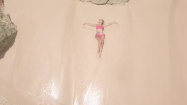 Havadan üstten kumlu plajda ve deniz dalgalarında bikinili genç kadın. Güzel kadın güneşleniyor ve deniz plajında dinleniyor ve kuma sıçrayan su dalgaları. Yaz seyahat konsepti.