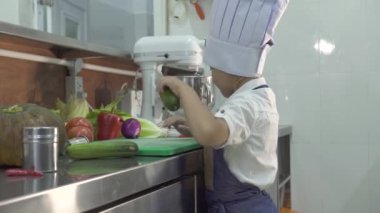 Küçük çocuk şef restoran mutfakta apron ve şef şapka pişirme yemek pişirin. Komik küçük aşçı ticari mutfakta ahşap tahta üzerinde taze sebze kesme. Çocuklar yemek pişiri.