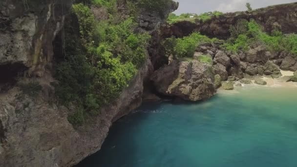 岩の多い海岸の空中風景の崖。海岸の岩の崖に飛び散る美しい青い海の波。ターコイズブルーの海水と岩の島のドローンビュー。バリ島,インドネシア. — ストック動画