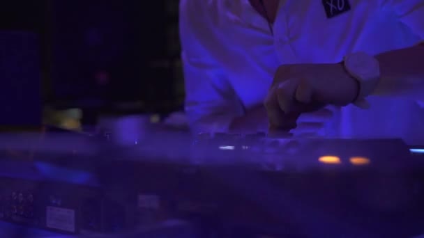 Man DJ παίζει μουσική σπίτι στην κονσόλα ήχου στο πάρτι στο κλαμπ χορού. DJ χειριστήριο για την ανάμειξη μουσικής και πολύχρωμο φως στο νυχτερινό κέντρο διασκέδασης. Δίσκος ταμπλό και κατάστρωμα ανάμειξης σε πάρτι χορού. — Αρχείο Βίντεο